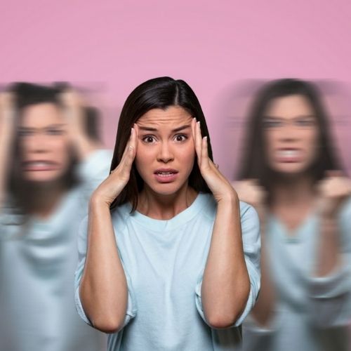 Žena v svetlomodrej košeli si drží hlavu, v pozadí sú rozmazané postavy tej istej ženy na ružovom pozadí, čo predstavuje emočnú nerovnováhu.