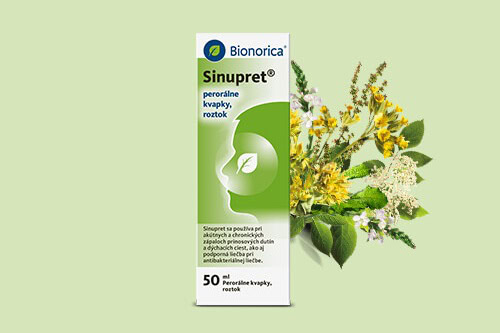 Krabička Bionorica Sinupret kvapiek s bylinkami v pozadí, posadená na svetlozelenom povrchu.
